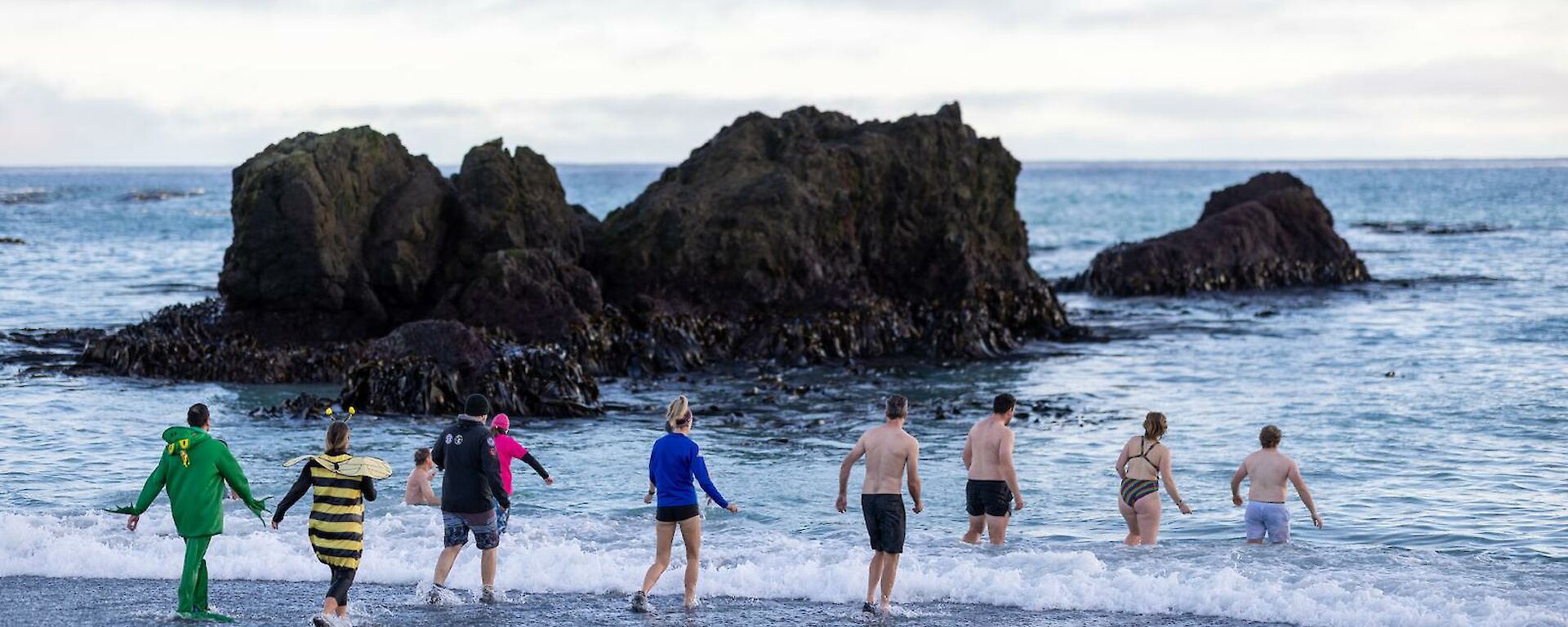 A group of people in colourful swimming attire run into the water on a beach.