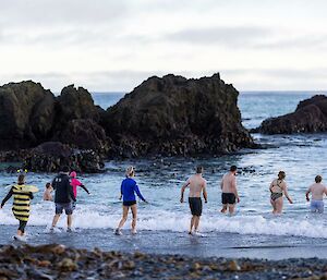 A group of people in colourful swimming attire run into the water on a beach.