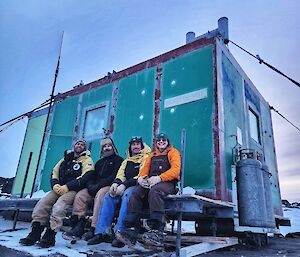 four people sitting on deck in front of hut