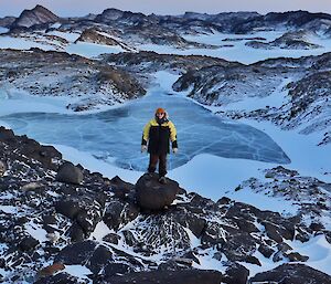 person standing on rock looking over frozen lake