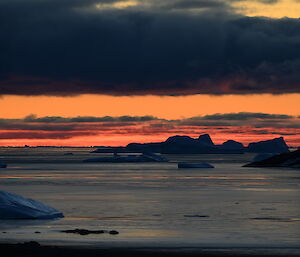 sunset on a still bay, with icebergs in the distance