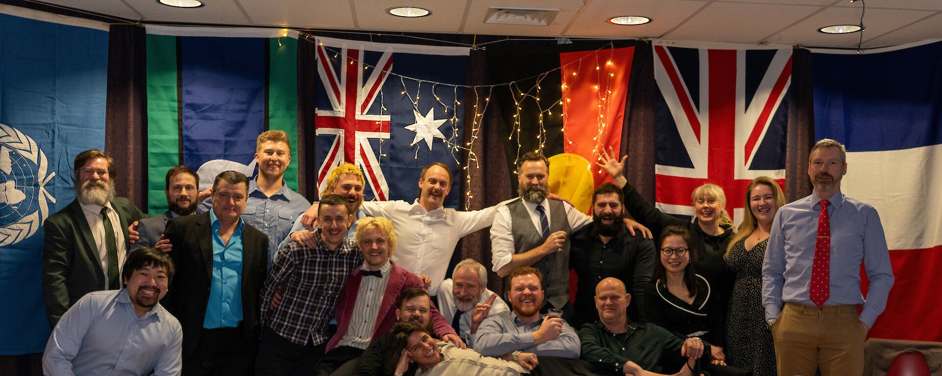 Group photo of expeditioners around a table with flags in the background