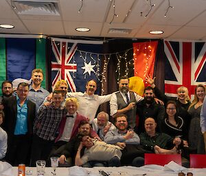 Group photo of expeditioners around a table with flags in the background