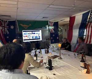 People sit around a table with flags hung all around, watching a TV