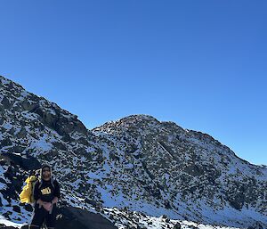 person standing next to rock under blue sky with snow all around