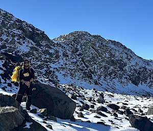 person standing next to rock under blue sky with snow all around