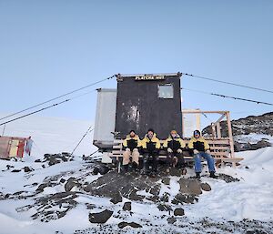 four people sitting on seat out the front of a hut