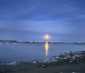 moon over a still bay, fringed with ice with the yellow moon in the distance