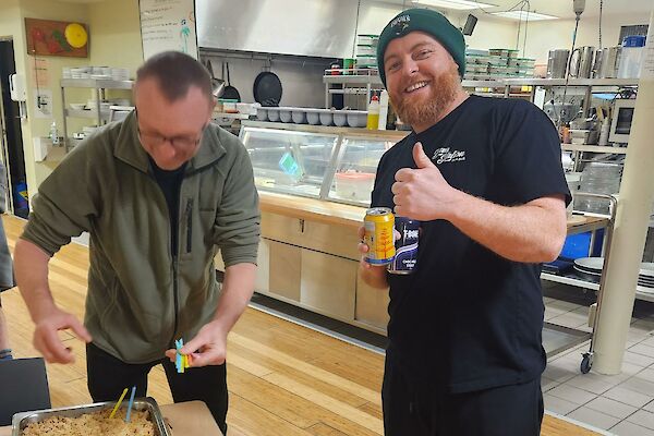 Two men stand in an cafeteria with a cake