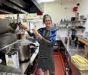 A smiling woman stands in a kitchen about to put two-minute noodles into a pot of boiling water