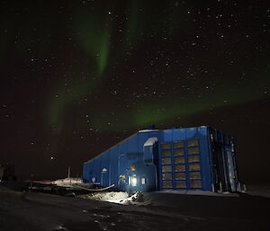 Green flickering light in a night sky over a blue shed