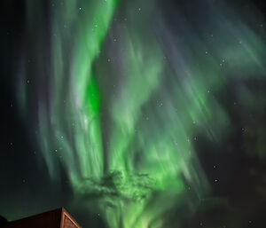 Very bright green lights dancing in ribbons in the night sky above a brown building