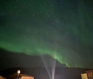 A star-studded night sky with a band of green light across it with buildings in the foreground