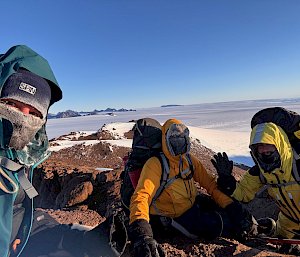 Three people sitting on rocks on tops of a mountain.