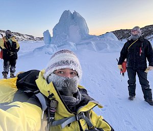 A selfie in front of a large iceberg/