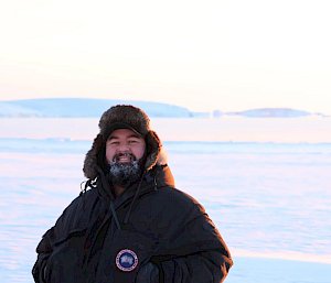 An expeditioner standing with an ice and snow background smiling to the camera