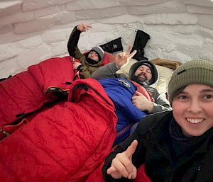 Three expeditioners looking happy and warm in their sleeping bags inside an igloo