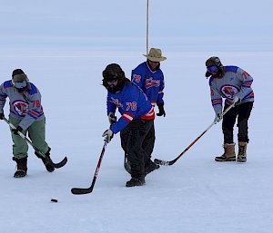 Four expeditioners dressed in matching blue and red jerseys playing ice hockey on the ice
