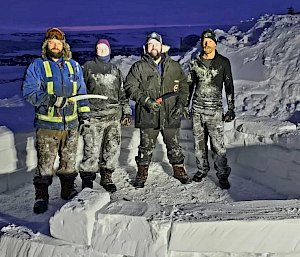 Four expeditioners stand in the base layers of an igloo