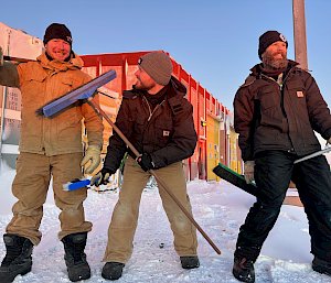 Three people standing next to each other with brooms