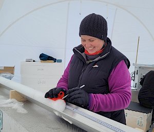 A woman uses a pencil to mark the end of an ice core.