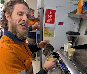 A man creates latte art on the top of a third coffee