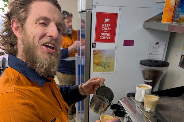 A man creates latte art on the top of a third coffee