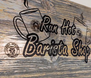 A wooden sign with Run Hot Barista Shop etched on it, alongside a picture of a mug and the station logo