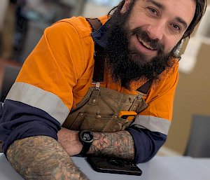 A man smiling at the camera, with a coffee in front of him and a crossword puzzle