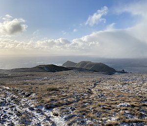 A snow-covered plateau in the foreground with hills and ocean in the distance