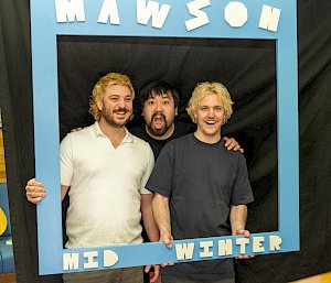 Three men standing inside a Mawson midwinter sign.