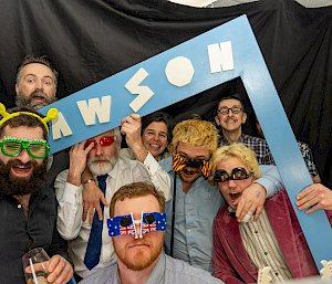 A group of people wearing party glasses arranged around a Mawson sign