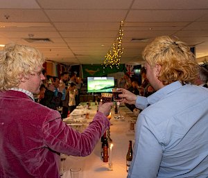 Two men standing at the head of a long table, chinking glasses.