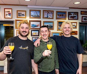 Three men raising glasses of orange juice. Two of them have blonde hair.