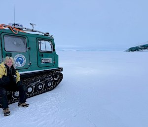 A man sitting on the wheel of a green haggland with a jade iceberg in the distance