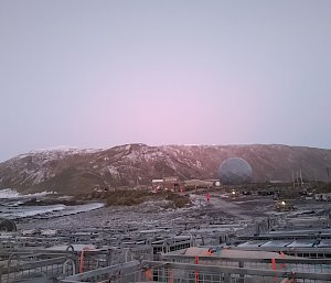 Looking out over numerous cage pallets to a giant blue ANARESAT dome, buildings and snow dusted hilltops in the distance.