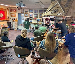 A group of people watching a man play darts