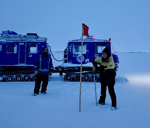 Two expeditioners outside in the snow and ice of Antarctica, in front of a tractor