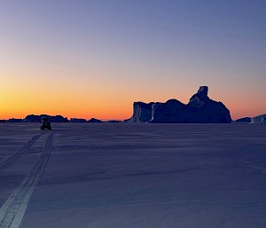 A tractor driving across the ice at sunset