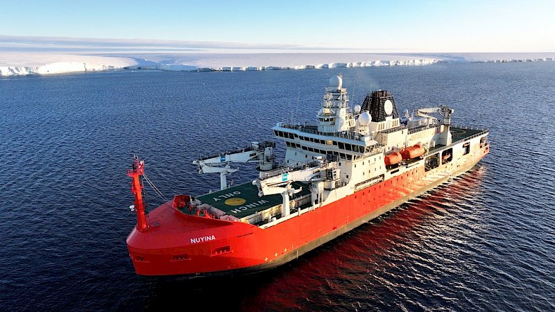 A big red and white ship in the ocean with white ice shelf behind it