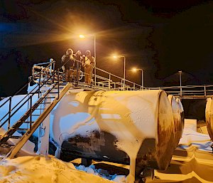 People stand on a walkway over fuel tanks, covered in snow