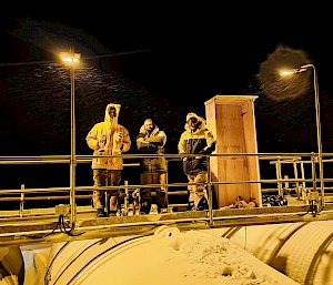 Three expeditioners standing outside at night in the snow