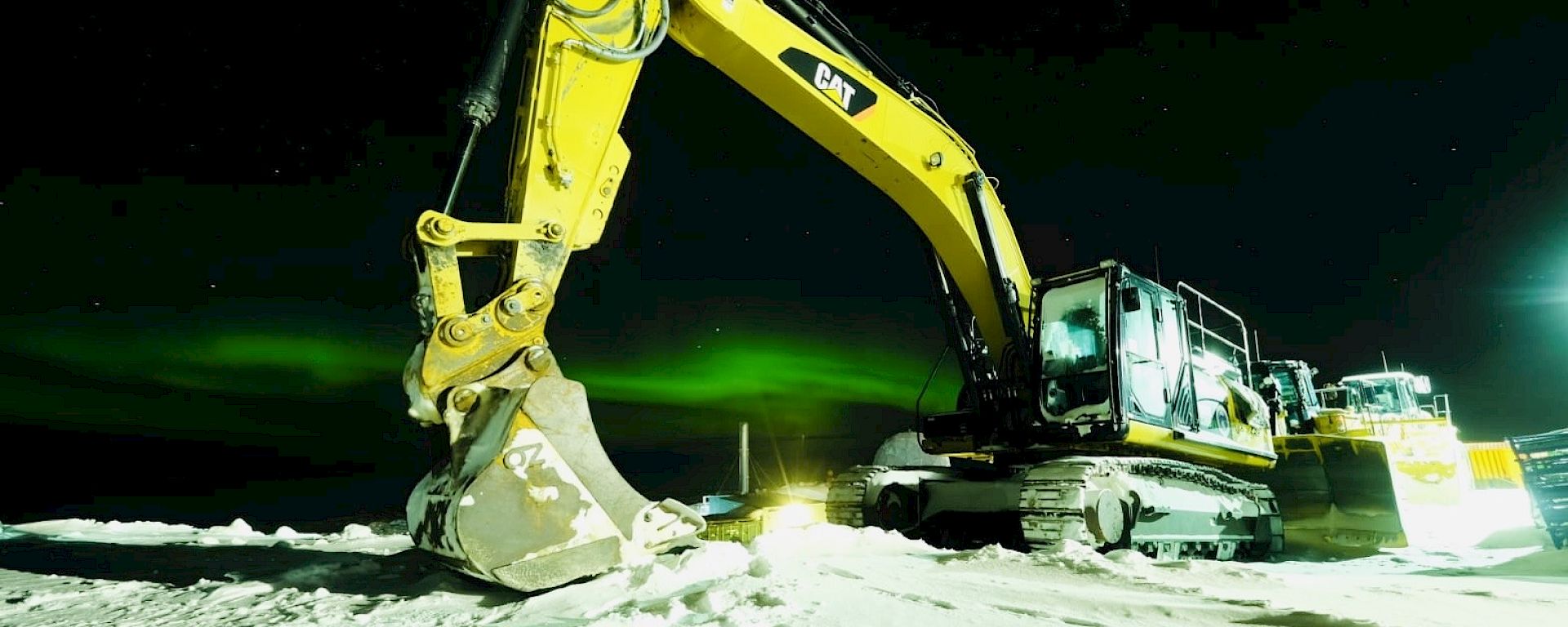 A piece of heavy machinery with the green lights of an aurora shimmering in the background
