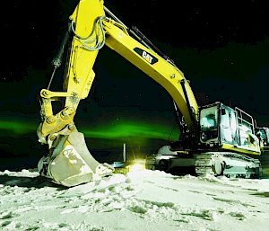A piece of heavy machinery with the green lights of an aurora shimmering in the background
