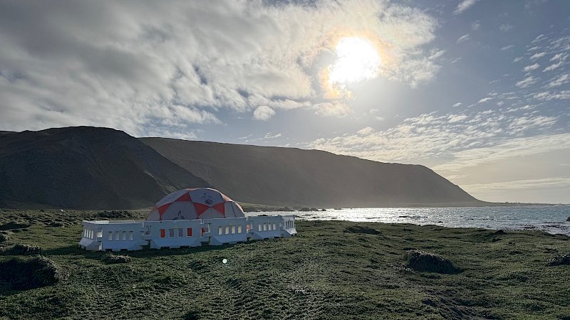 An orange and white dome tent with a white plastic fence around it on a remote island