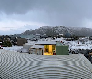 A panoramic photo of a snow-covered landscape with buildings in the foreground, ocean on either side and snow-covered mountains in the background.