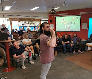 A man standing in front of a crowd with his arm pulled back, ready to throw a dart.