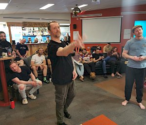 Two men standing in front of a crowd. One man is mid-way through throwing a dart.