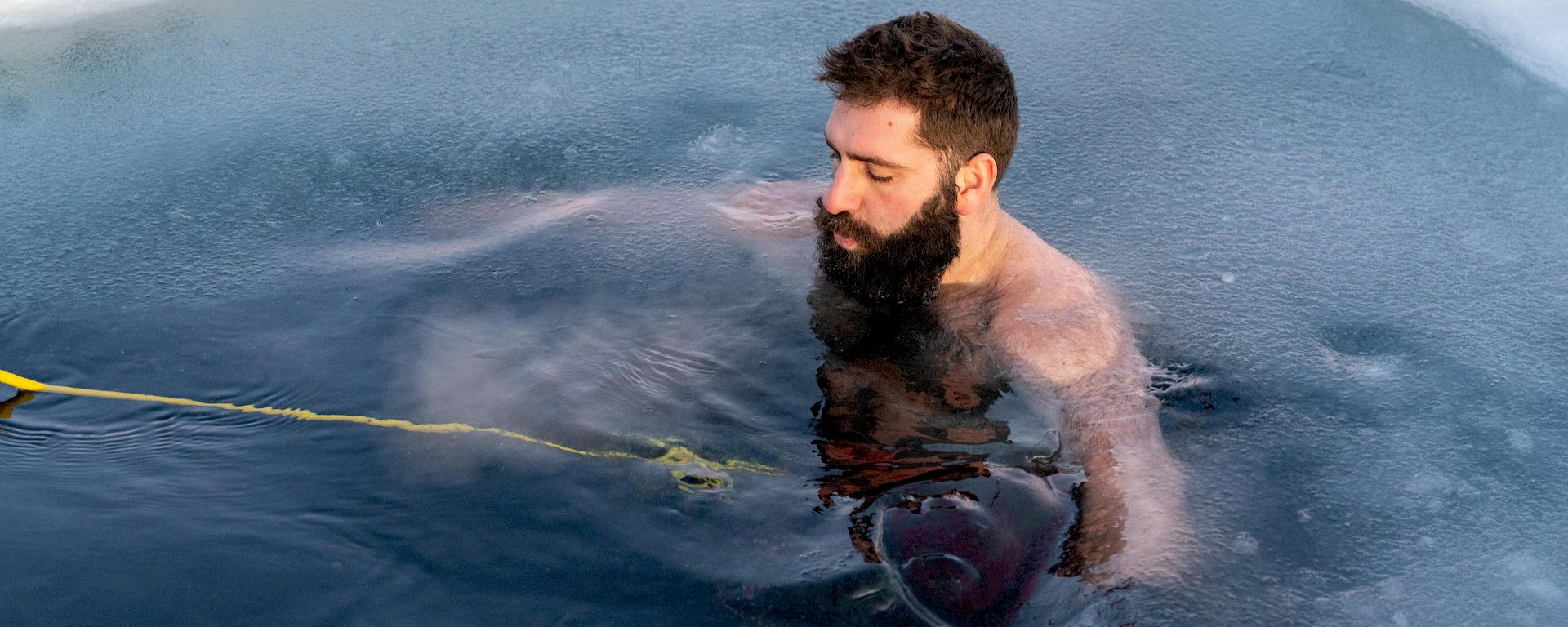 A man floating in a hole in the sea ice. He is attached to a rope.