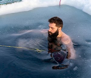 A man floating in a hole in the sea ice. He is attached to a rope.